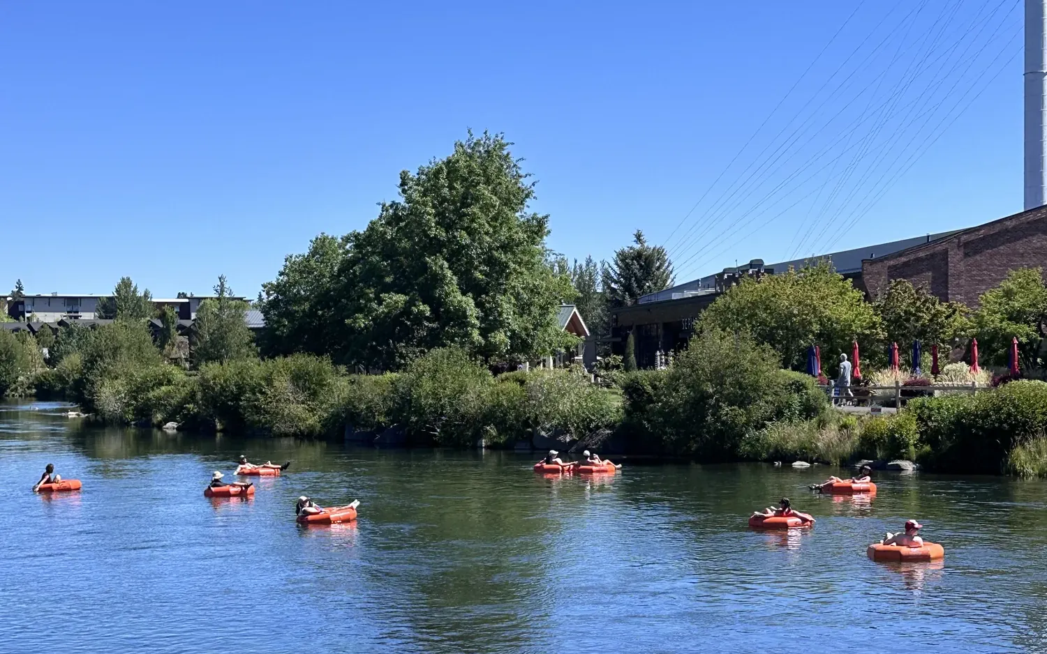 People floating the Deschutes River in orange tubes past the Old Mill District in Bend on a sunny summer day
