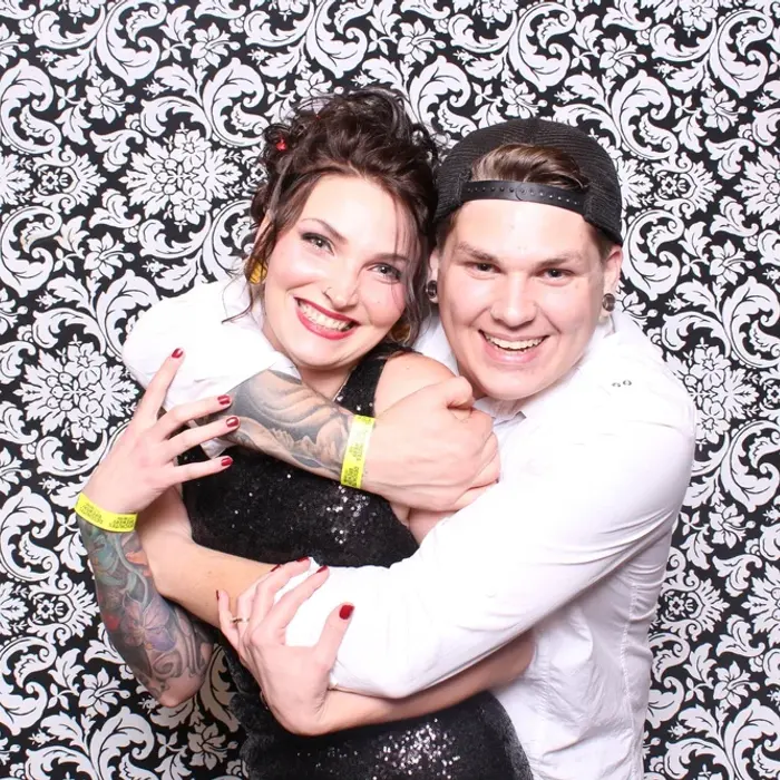 Two guests hugging and laughing in front of a black-and-white damask backdrop