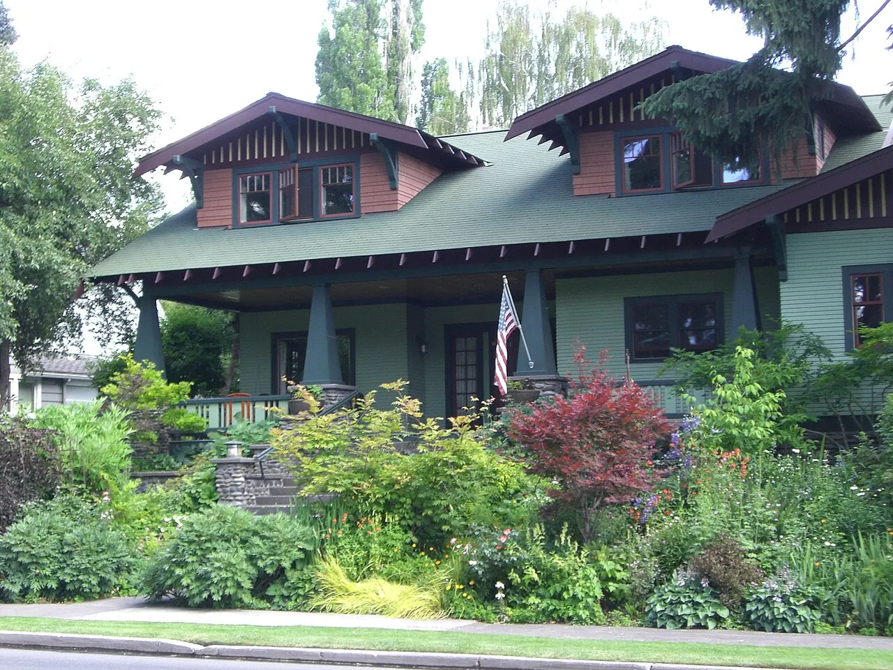 A green Craftsman bungalow with a deep porch and a garden of shrubs and perennials in Bend’s Drake Park neighborhood