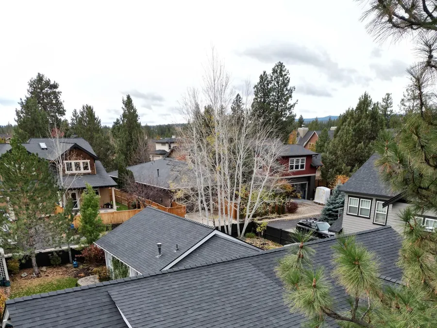 Aerial view of a new dark gray shingle roof on a Redmond house surrounded by pine trees and neighboring homes