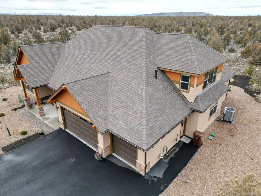 Aerial view of a large hip roof with gray shingles on a two-story house in the Sisters area with junipers and a paved drive