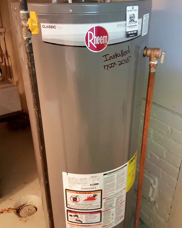 A newly installed gray Rheem gas water heater with its vent pipe and copper water lines