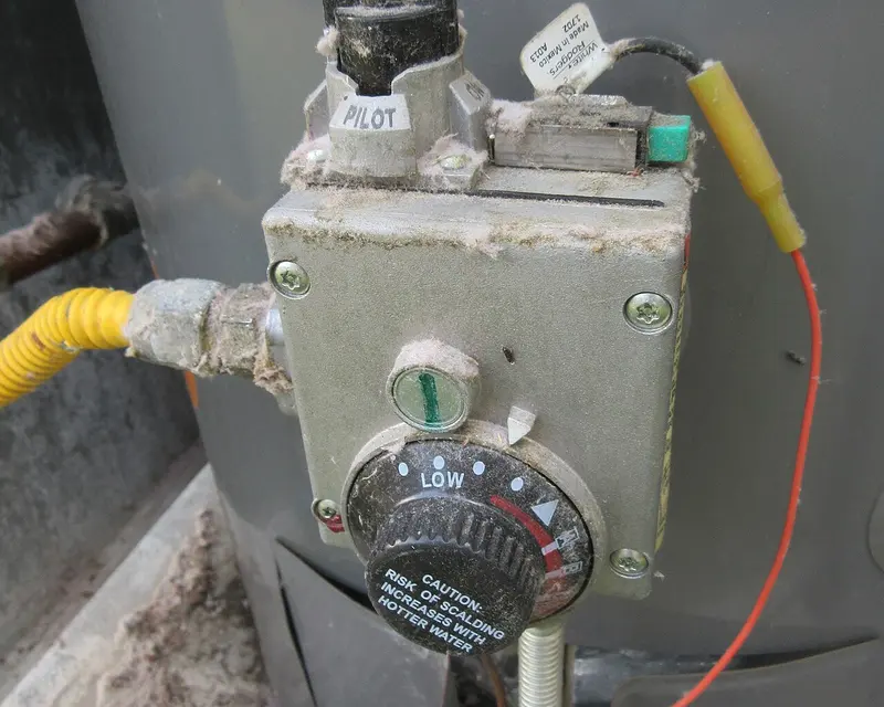 Close-up of a gas water heater control valve with a temperature dial set between low and hot and a pilot igniter button