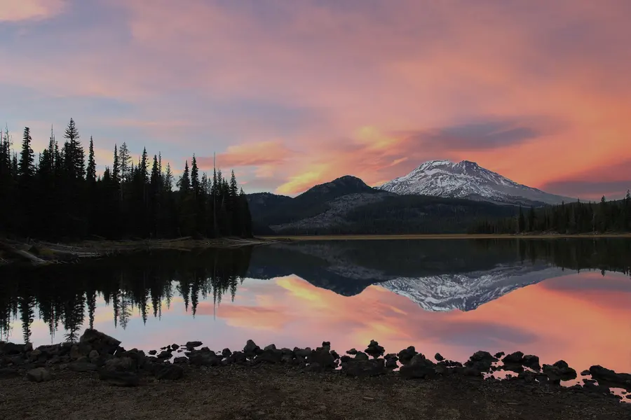 South Sister and Broken Top reflected in still Sparks Lake under a pink sunset