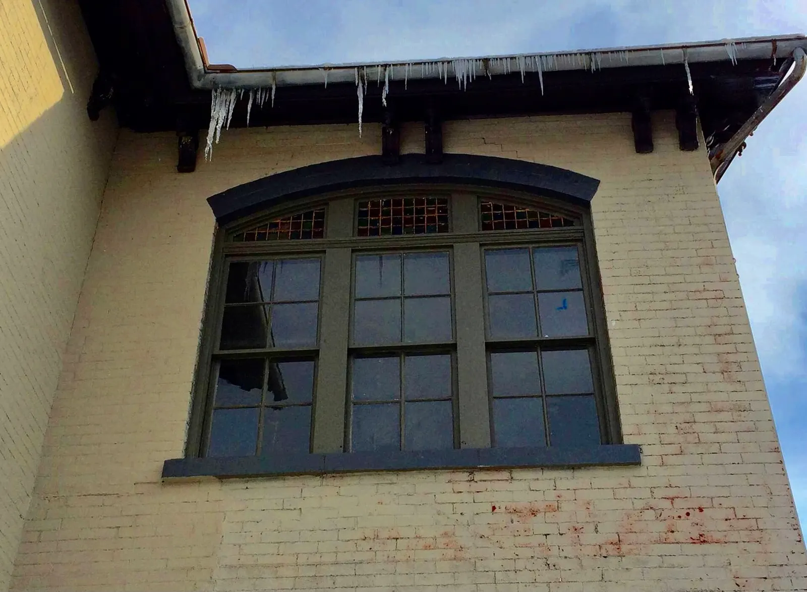 Long icicles hanging from a gutter along the eave of a brick house in winter