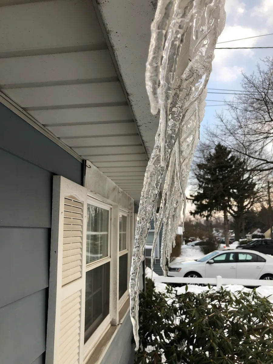 Thick icicles hanging from a white rain gutter on a house