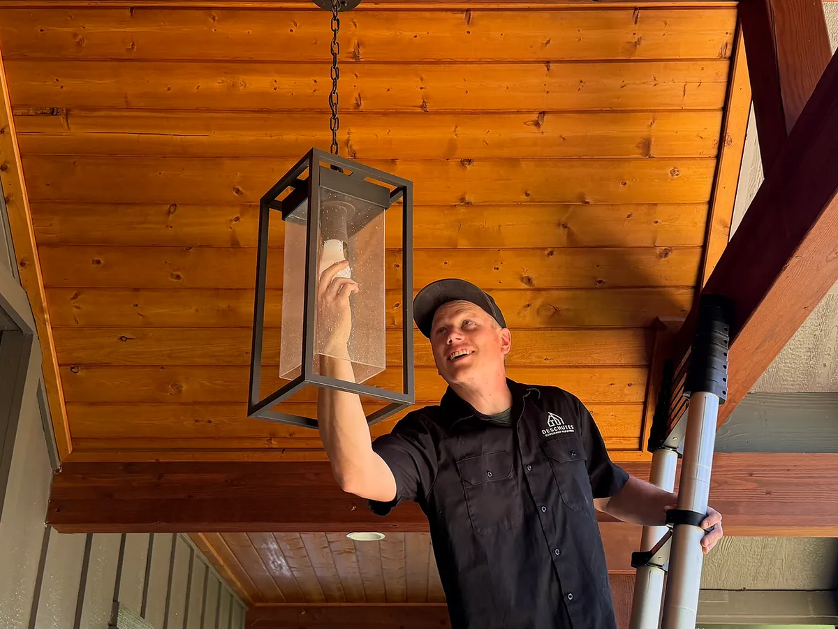 A Deschutes Concierge Handyman technician installing a porch light under a wood ceiling