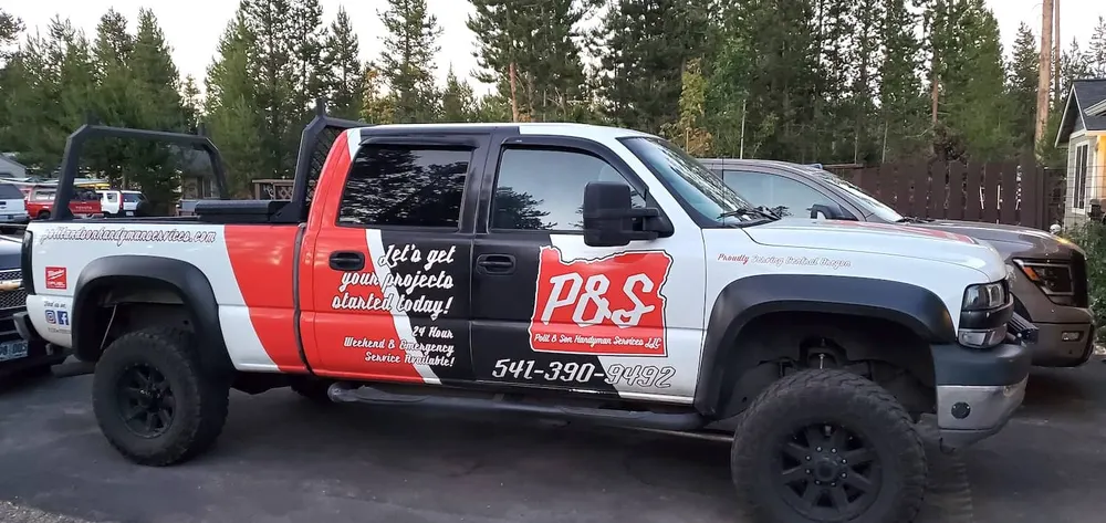 The red and white Polit & Son Handyman Services truck parked among pine trees
