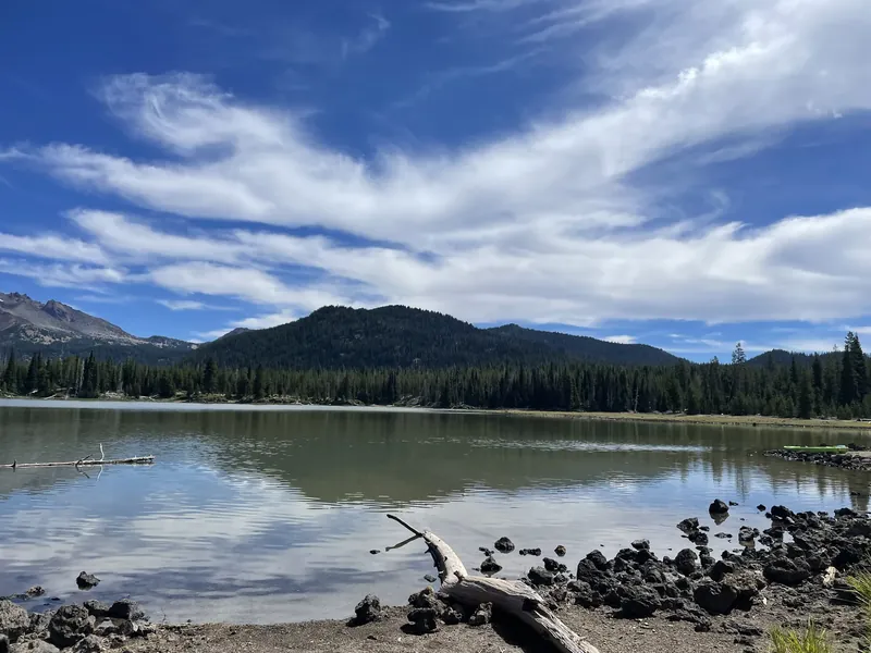 A Cascade lake with a forested butte and clouds behind it