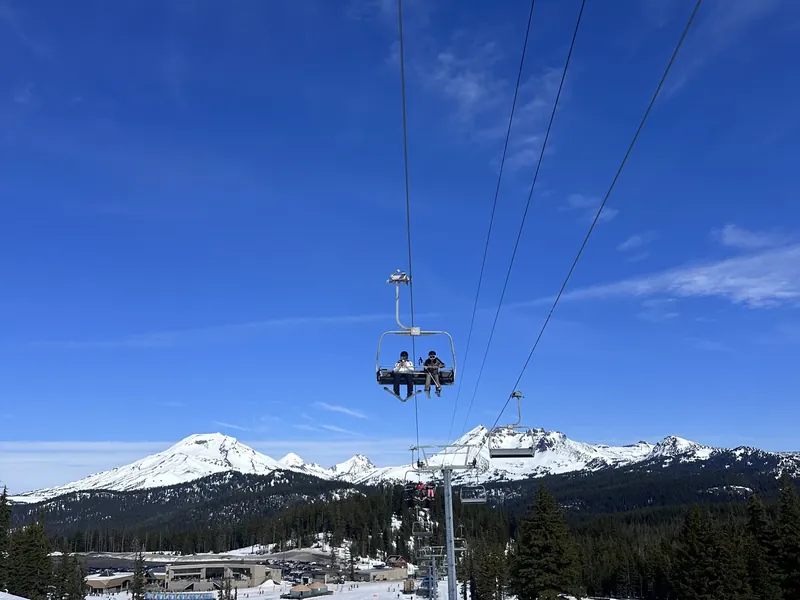 A chairlift at Mt. Bachelor with snowy peaks behind it