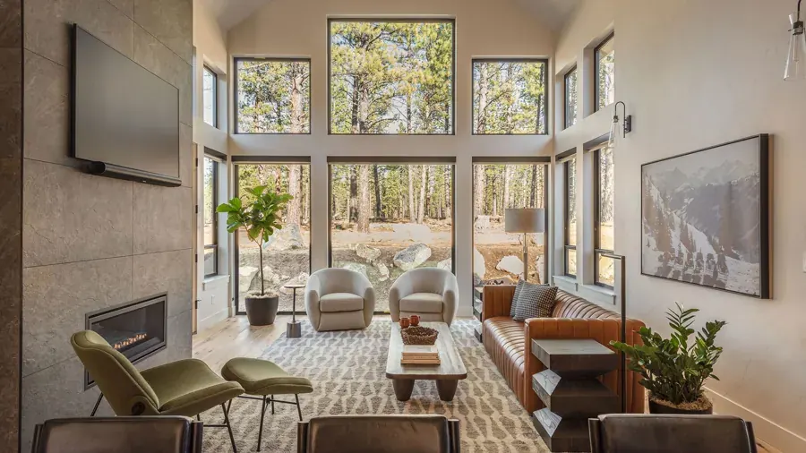 A tall living room with a wall of windows looking into pines, by Amy Troute Inspired Interior Design