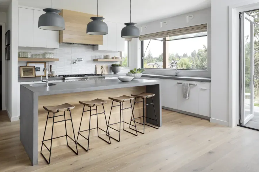 A modern kitchen with a concrete island and pendant lights by Harper House Design in Bend