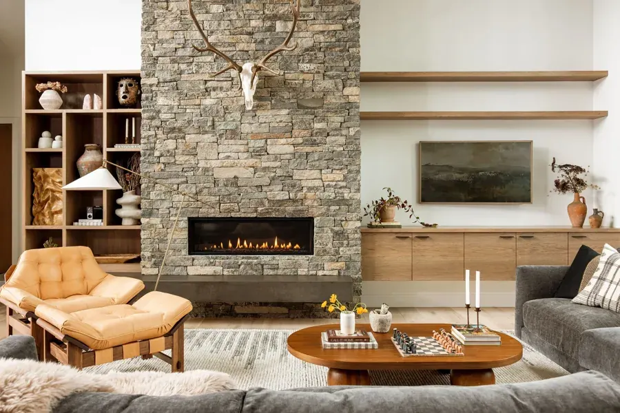 A living room with a stacked stone fireplace and wood built-ins by House of Milo in Bend