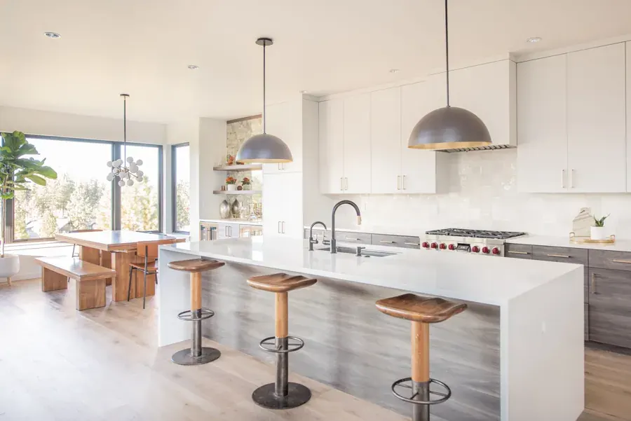 A bright kitchen with a long island and dome pendants by KMR Interior Design in Bend