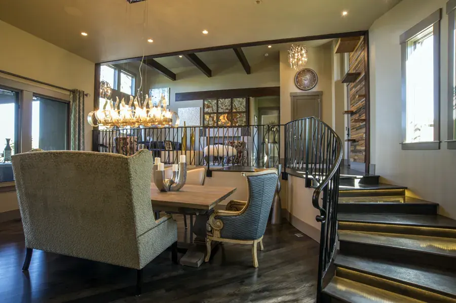A dining room with a long chandelier and stair by L. Hendrix Interiors in Central Oregon