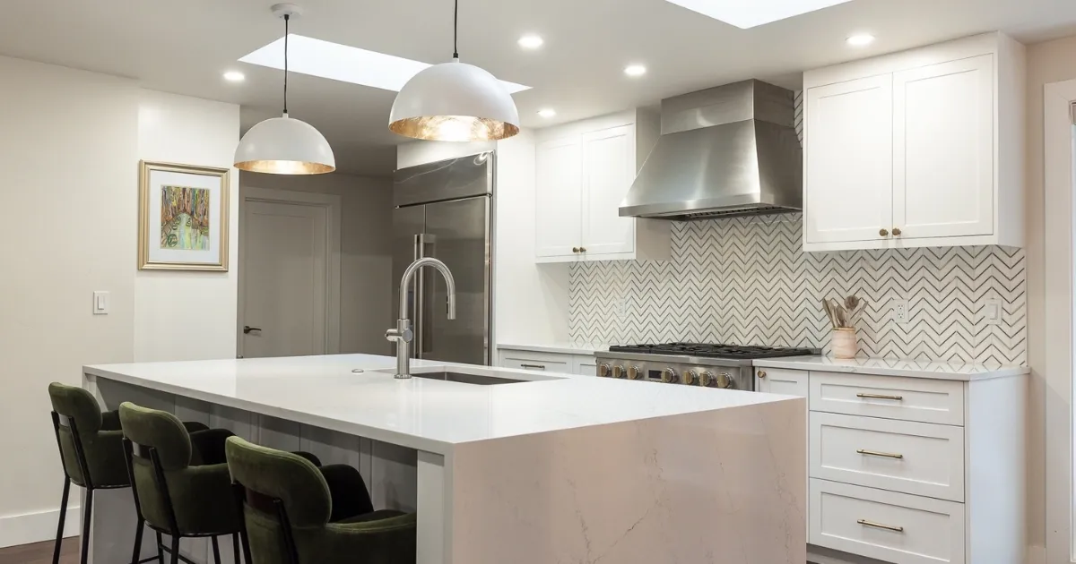 White kitchen with a large island and stainless hood by Appel Design & Construction