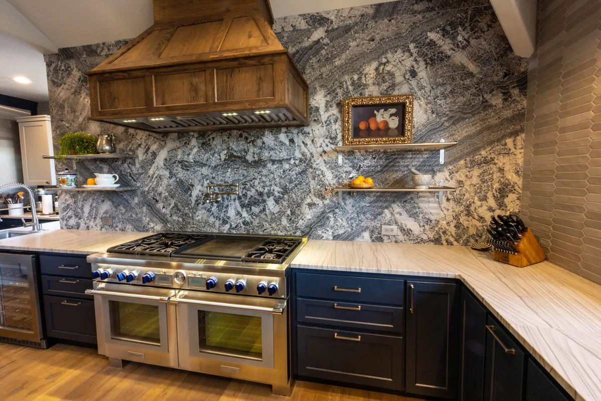Kitchen with a dramatic stone backsplash, copper range hood and navy cabinets by K2 Design Remodel