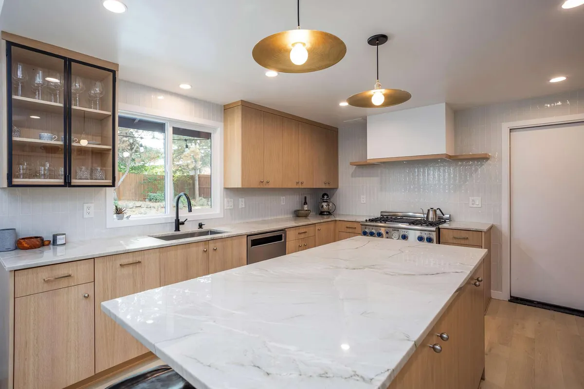 White oak kitchen with a marble island and brass pendants by Linnius Construction