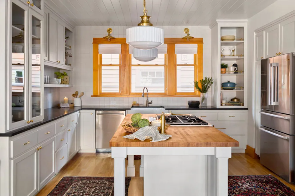 White kitchen with a butcher block island and brass lights by Sierra James Construction