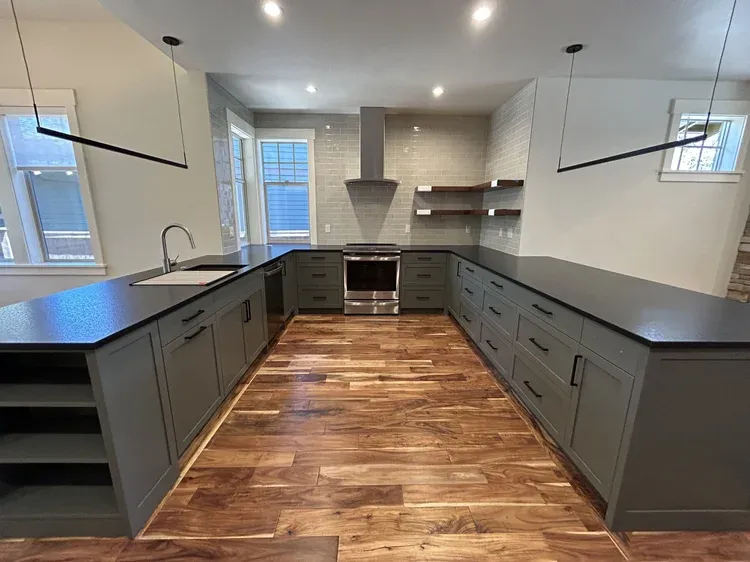 Dark cabinets with a wood floor and long counters by SRC Design & Build