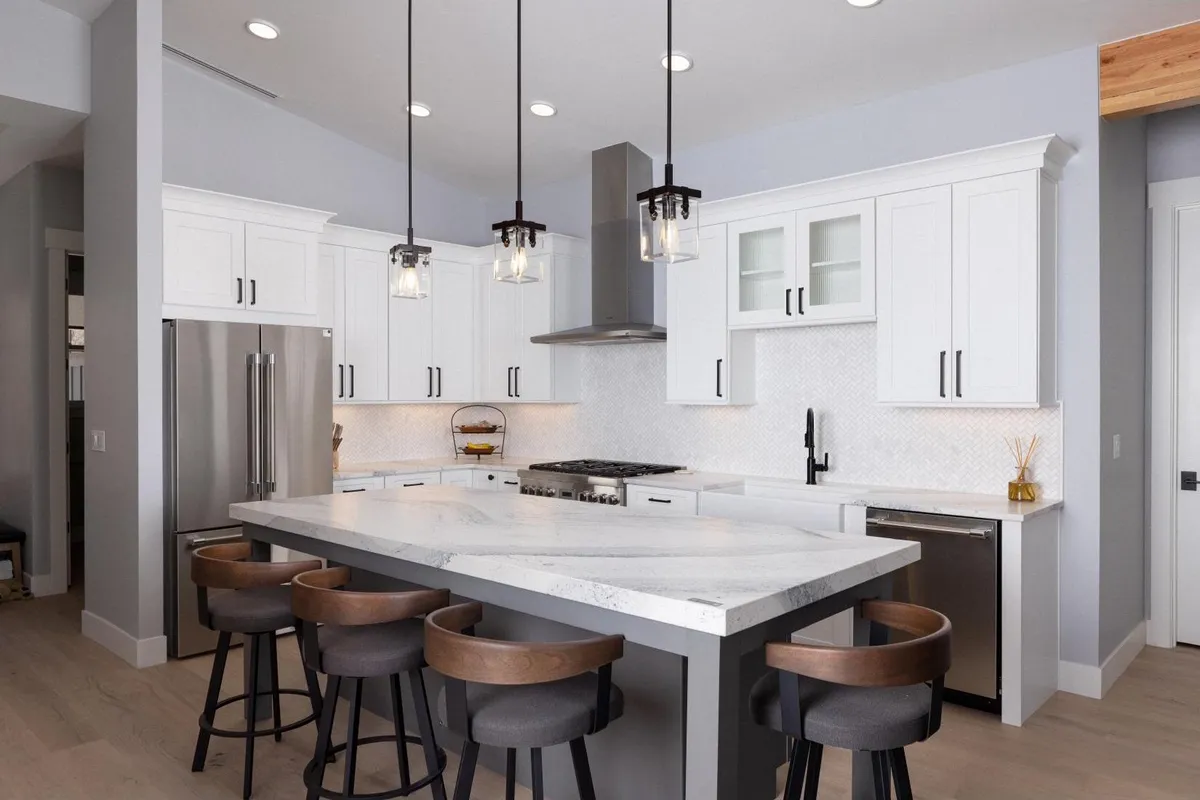 White kitchen with a large quartz island and black pendant lights by Surface Kitchen & Bath