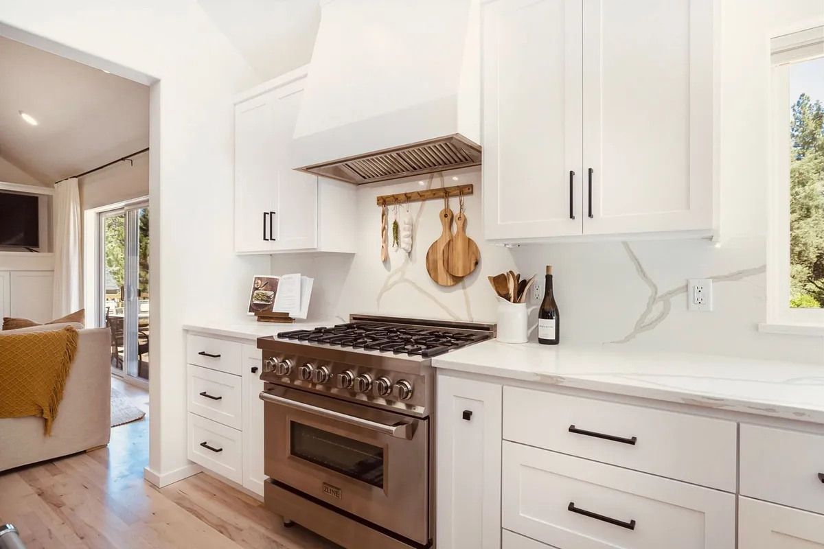 White kitchen with a professional range and pot rail by Total Home Solutions