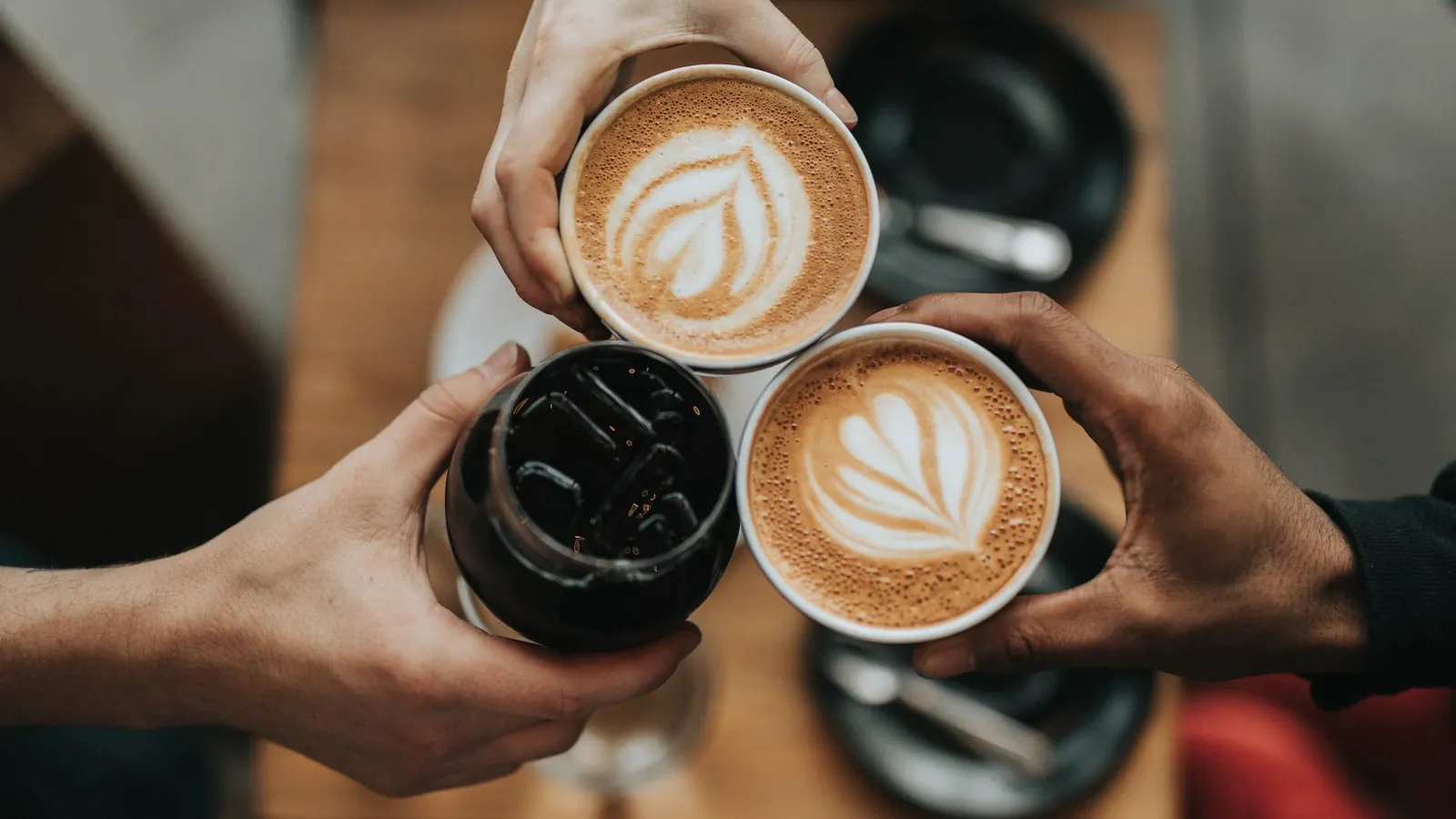 Friends clinking lattes and an iced coffee at a Bend café table