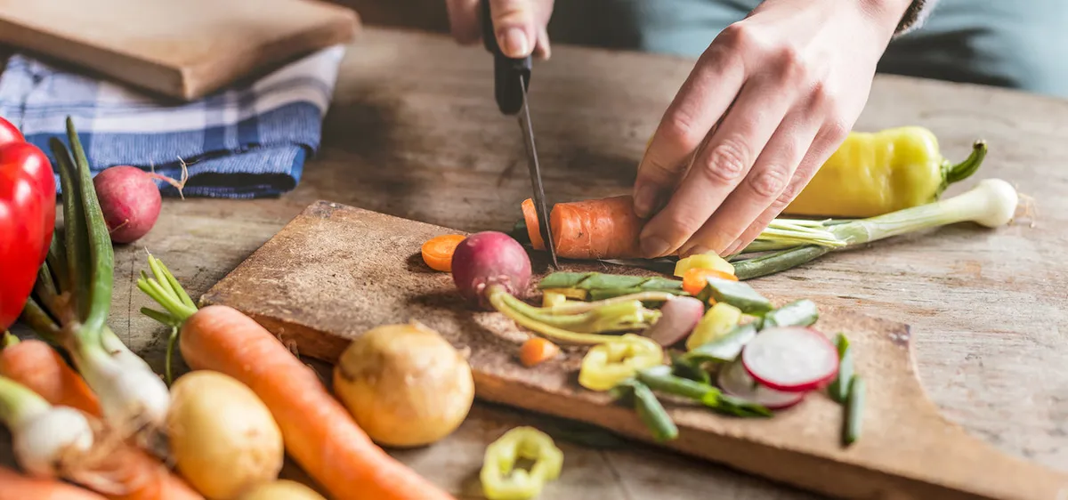 A chef chopping fresh carrots, radishes and peppers on a wooden board