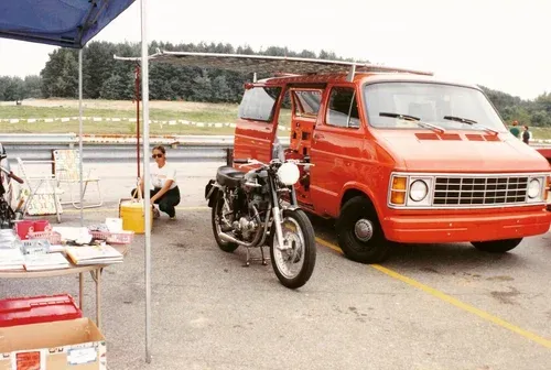 A vintage motorcycle and an orange van at a 6 Volt Cycles event