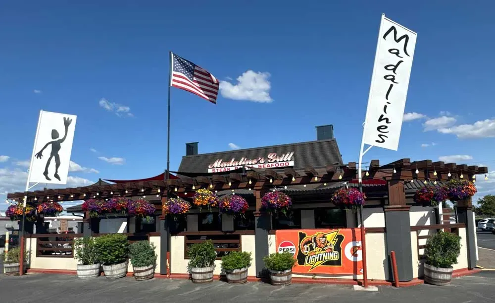 The outside of Madaline’s Grill & Steakhouse in Redmond with flags and flower baskets