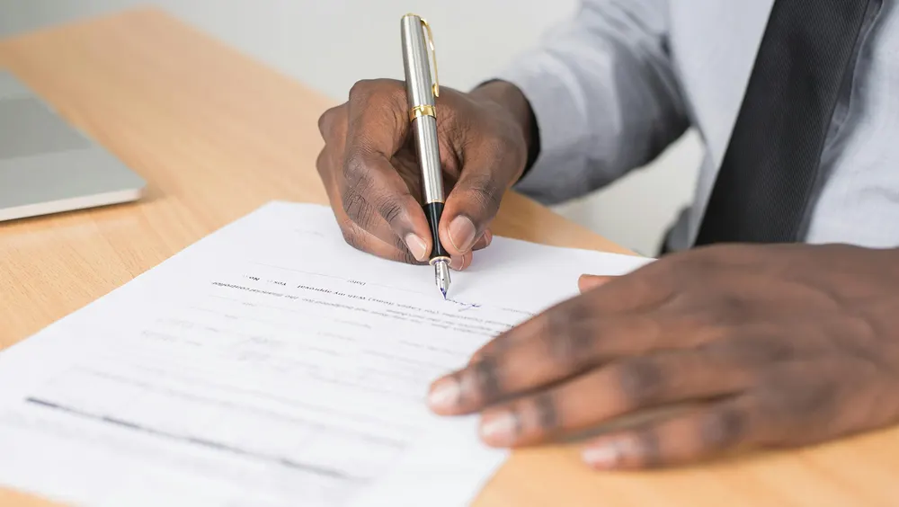 Person signing a document with a pen