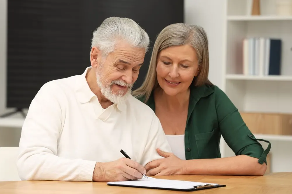 Older couple signing documents at their kitchen table
