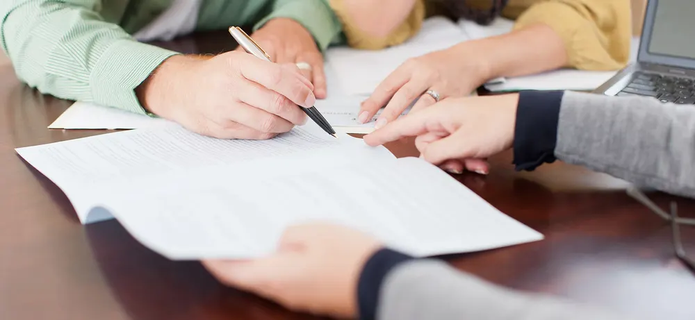 Two people signing paperwork across a table