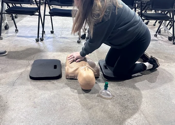 Person kneeling on a foam pad practicing chest compressions on a manikin during CPR training in Bend, Oregon