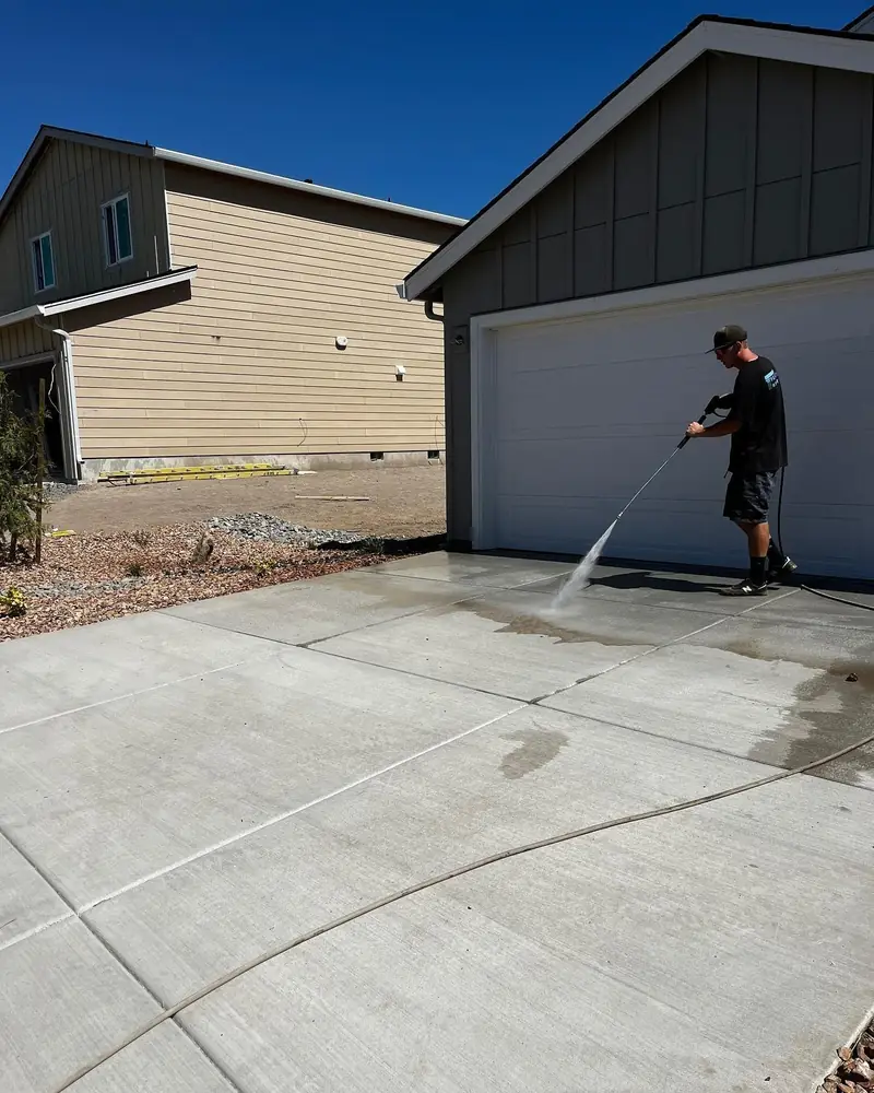 A worker pressure washing a new concrete driveway in front of Central Oregon homes