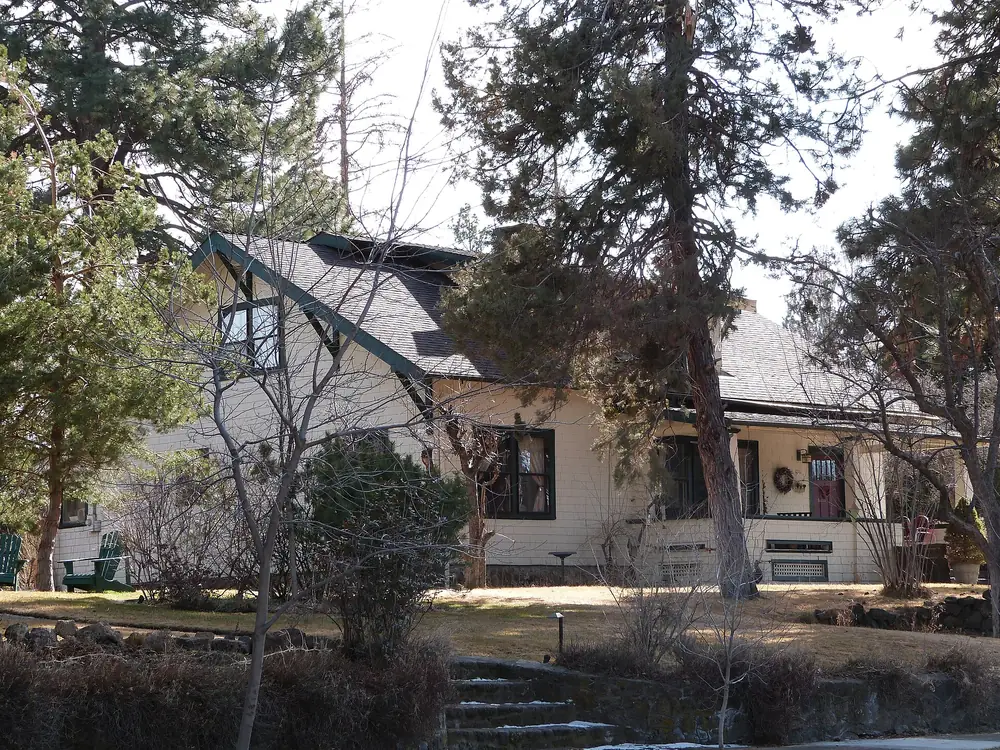 A house in Bend under tall ponderosa pines with a lava-rock wall