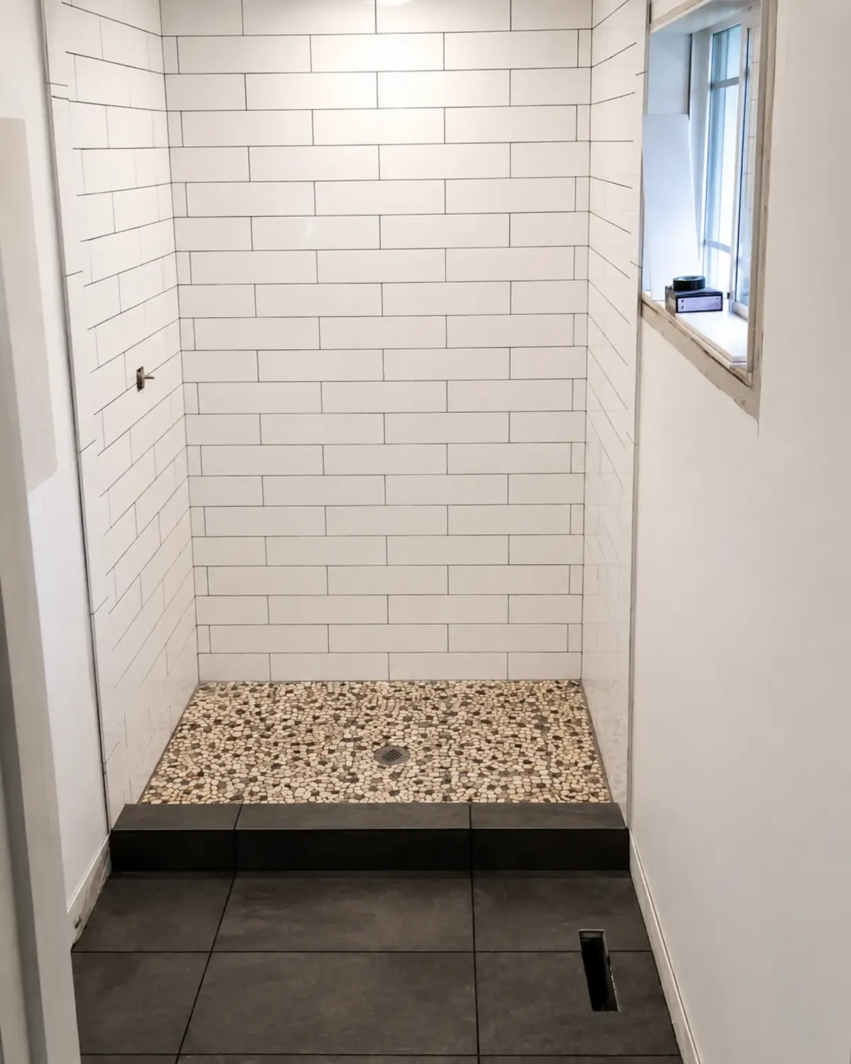 White subway tile shower with a pebble floor by Almog Construction
