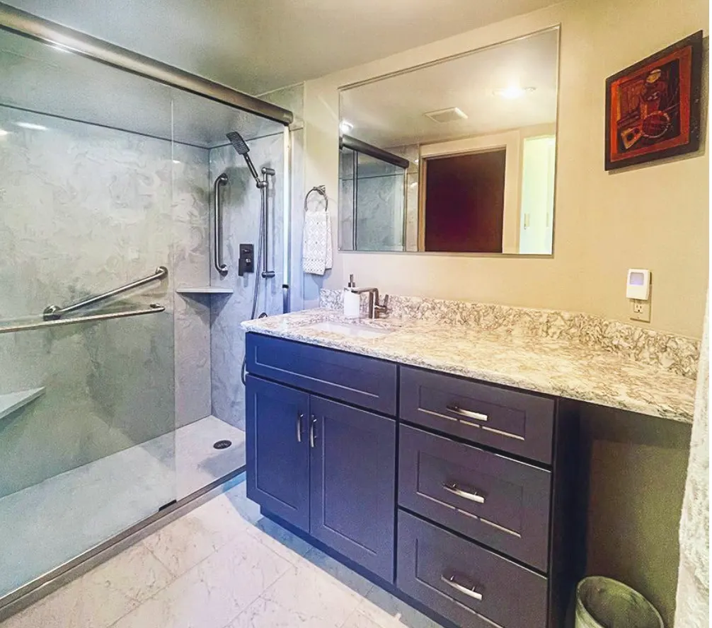 Low-threshold walk-in shower with grab bars and a dark vanity by Bath Techs