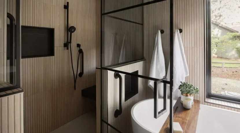 Warm contemporary Bend bathroom with wood slat walls, a black-framed shower and a soaking tub by Neil Kelly