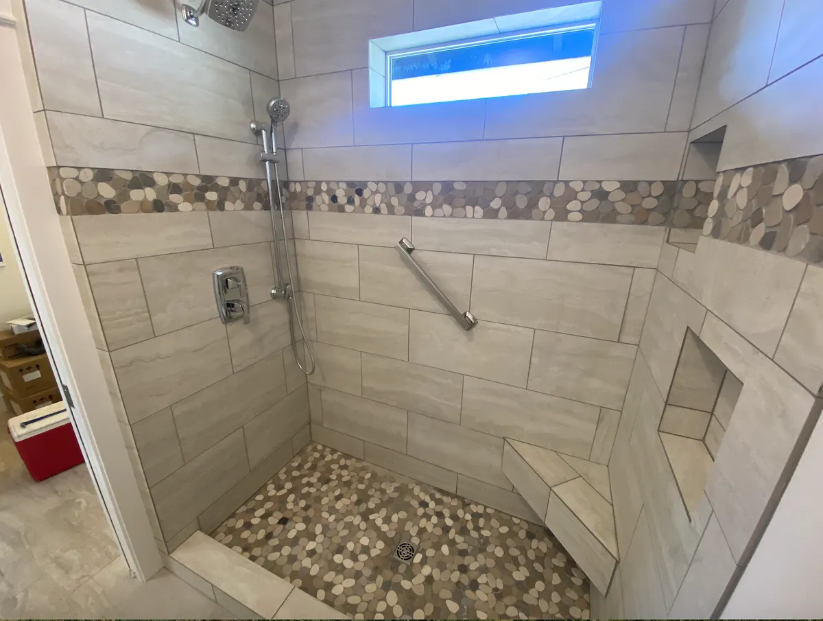 Walk-in shower with large gray tile, a pebble floor and a built-in bench by Rockin’ K General Contracting