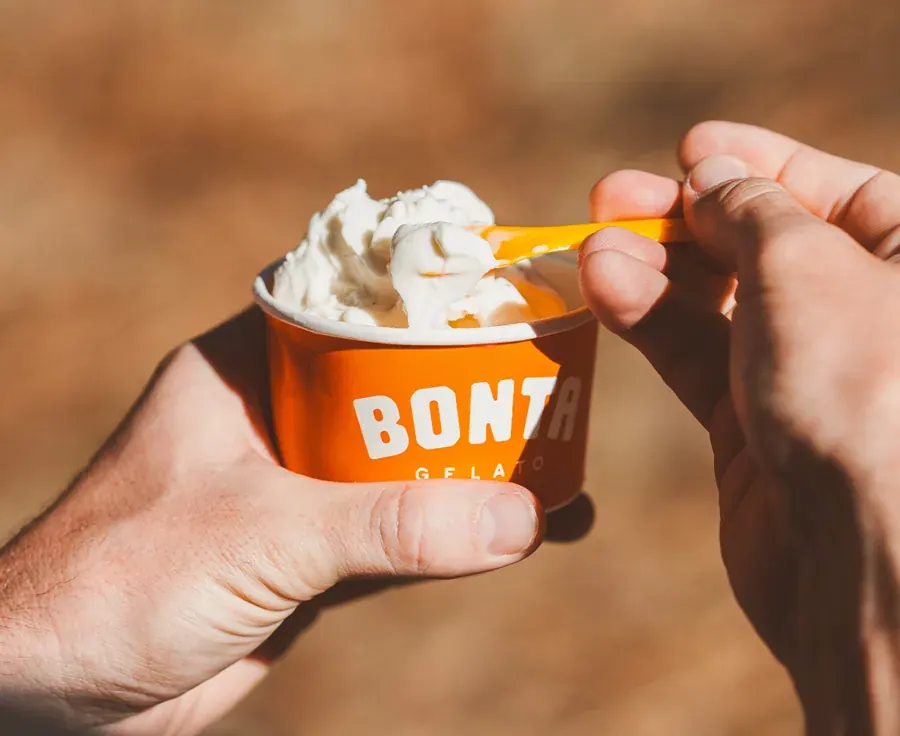 A hand holding an orange cup of Bonta gelato topped with cream