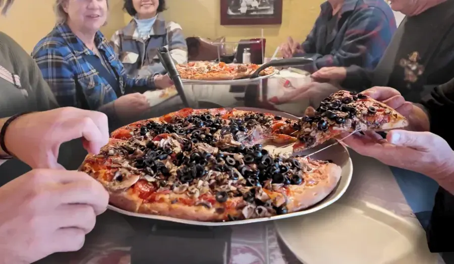 A table sharing a loaded pizza at Olde Towne Pizza on Greenwood Avenue in Bend