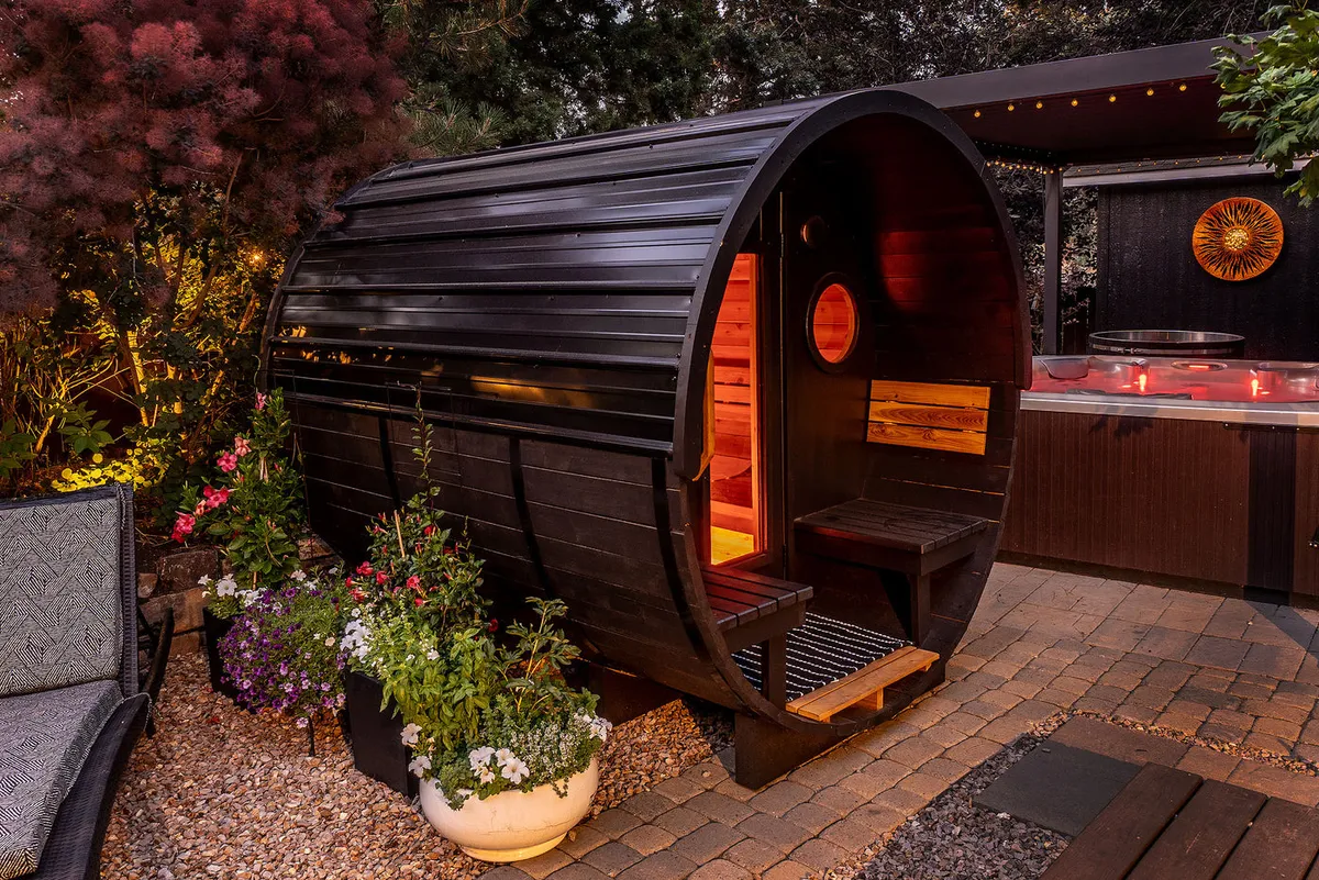 A cedar barrel sauna glowing at night on a backyard patio