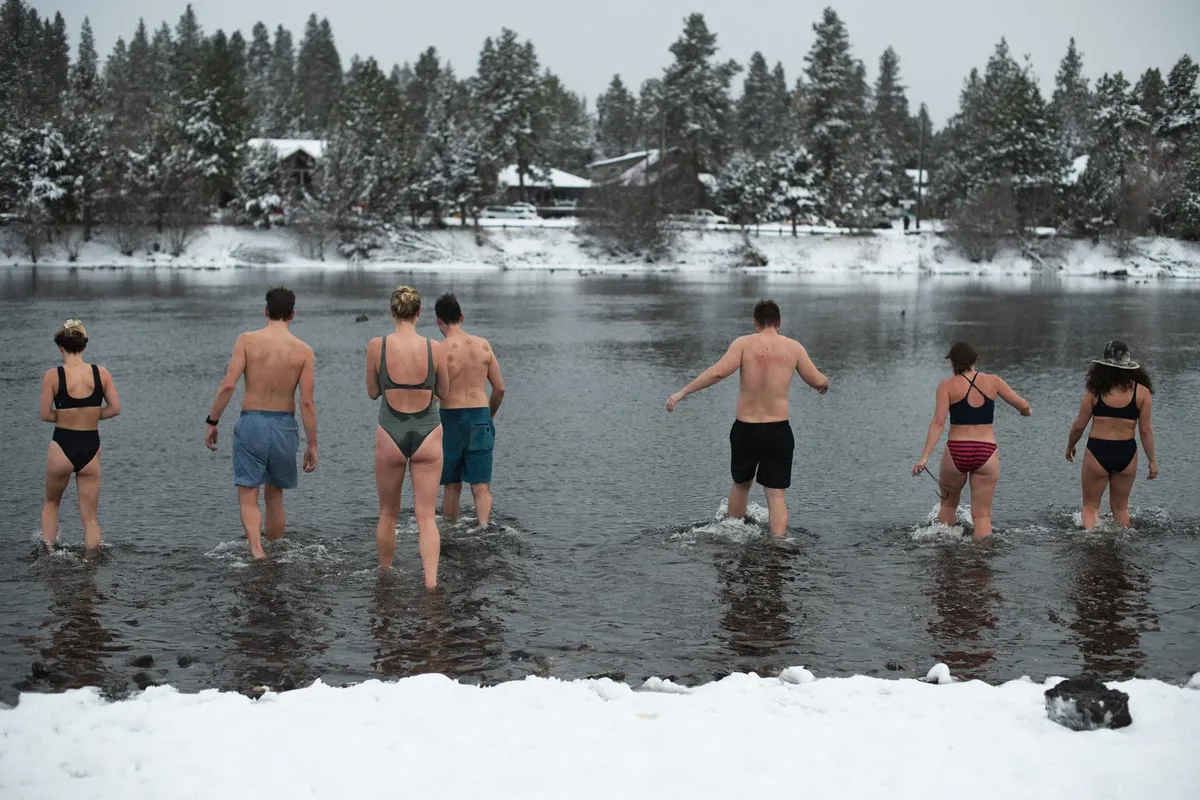 Sauna-goers wading into the snowy Deschutes River between wood-fired sauna rounds
