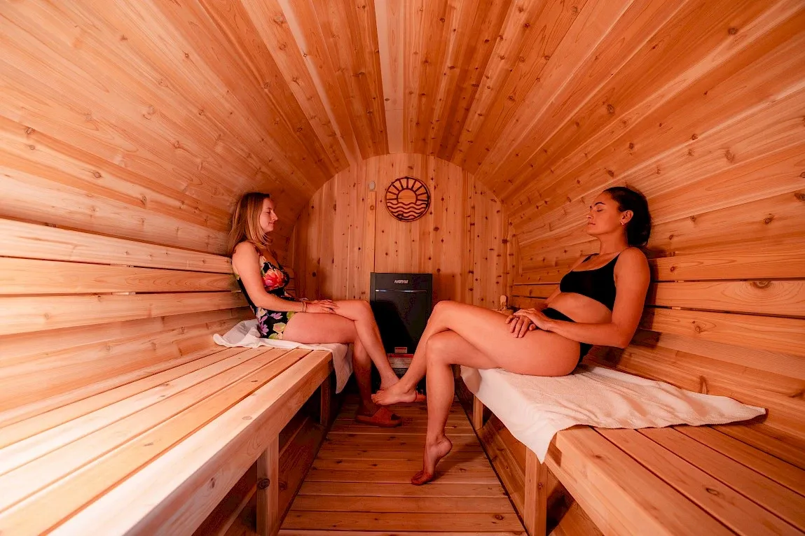 Two people relaxing in a cedar barrel-shaped sauna at Riverhouse Lodge
