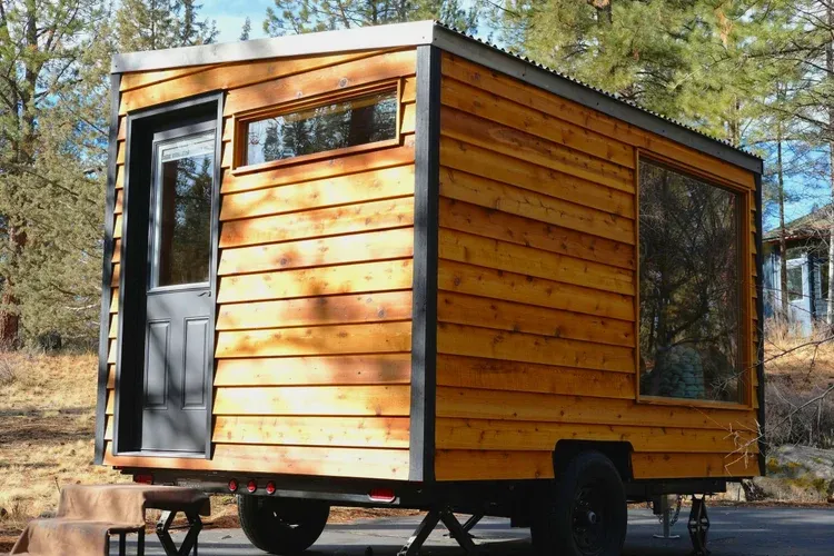 A shingled mobile sauna on a trailer among pines