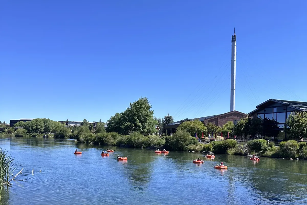 People floating the Deschutes River past the Old Mill District smokestacks in Bend, Oregon