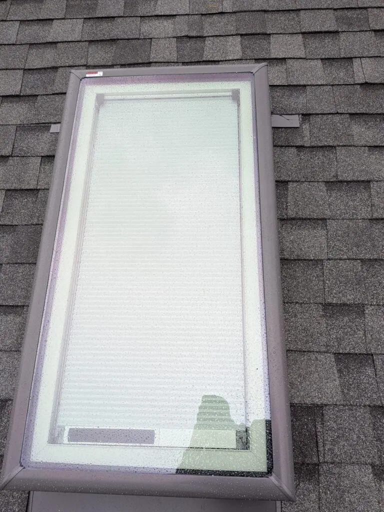 A new flashed skylight with a built-in shade on a gray shingle roof