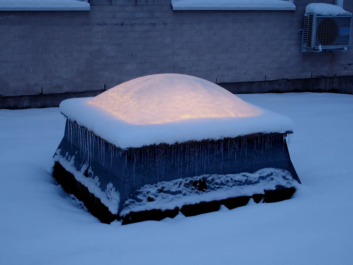 A skylight dome on a flat roof covered with a thick cap of snow