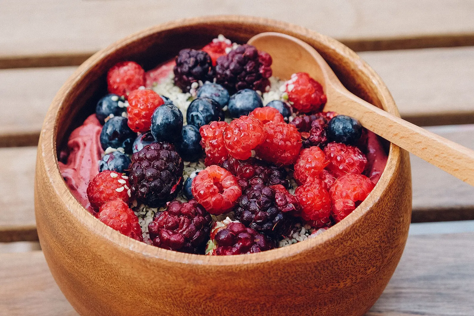 An açaí bowl piled with raspberries, blackberries and blueberries in a wooden bowl